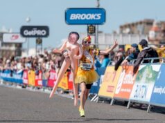 Woman dressed as chicken holds lifesize blow up doll with her own face on it, as she sprints towards finish line