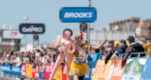 Woman dressed as chicken holds lifesize blow up doll with her own face on it, as she sprints towards finish line