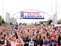 A large crowd of people cheer for the camera at the start line of the Manchester Marathon which reads Welcome and Good Luck