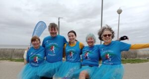 5 ladies dressed in blue T-shirts and tutus do the can-can