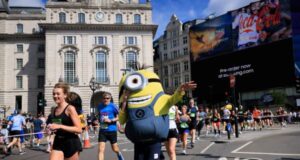 Peron dressed up as a minion runs alongside a female runner in black on a London street