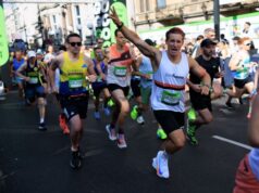 Runners on a busy street wave at the camera