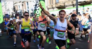 Runners on a busy street wave at the camera