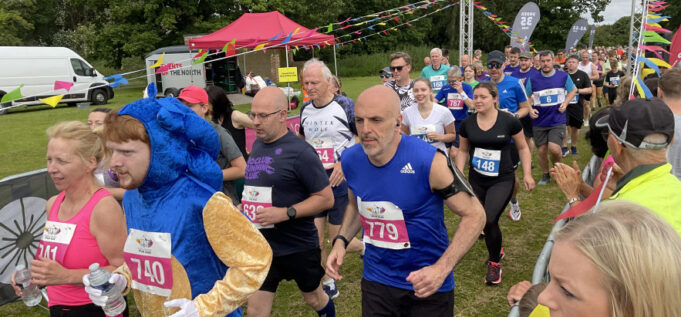 Runners in a race on grass all wearing pink race numbers