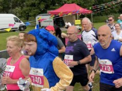 Runners in a race on grass all wearing pink race numbers