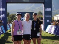 Three women smiling at a finish line, two of them wearing medals