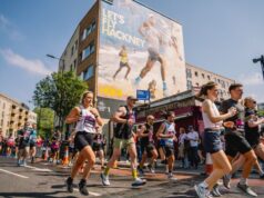 Runners in a race run by a wall painted with a running image saying Let's Fly Hackney