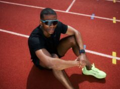 Man wearing sunglasses and dressed in running kit sits on track