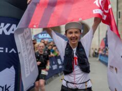 Female trailrunner crosses finish line with huge smile, and finish tape above her head.