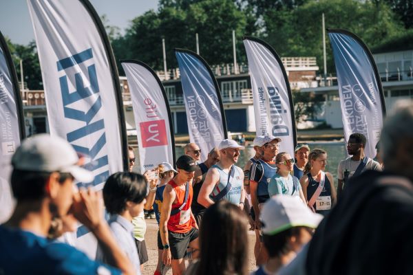 Runners wearing sashes line up at a start lined with flags