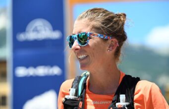 Woman in sungalsses, orange T-shirt and ultra vest smiles.