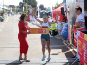 Barry Island 10K 2026 athlete preview Woman runs through finish tape of race with arms held high, while another woman in a red dress holds the tape for her