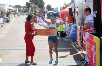 Barry Island 10K 2026 athlete preview Woman runs through finish tape of race with arms held high, while another woman in a red dress holds the tape for her