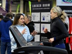 A woman standing at an expo chats to a woman on a treadmill