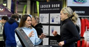 A woman standing at an expo chats to a woman on a treadmill