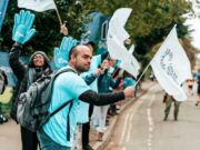 People in pale blue t-shirts and waving big blue hands cheer on runners at a road vent