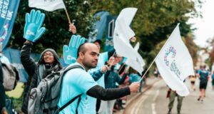 People in pale blue t-shirts and waving big blue hands cheer on runners at a road vent