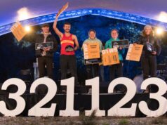 Three men and three women stand on a stage in front of large numbers 321123, some of them waving large cardboard Golden Tickets