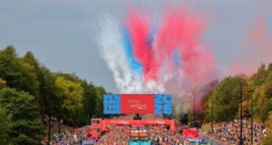 An explosion of red, white and blue from the Red Arrows fills the sky above runners on a dual carriageway
