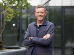 Man in suit jacket folds arms and smiles at camera