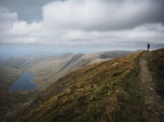 A sole runner atop a hill in an empty mountain scape with a lake visible in the background