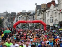 Many runners at the start line of a race under a red inflatable gantry