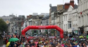 Many runners at the start line of a race under a red inflatable gantry