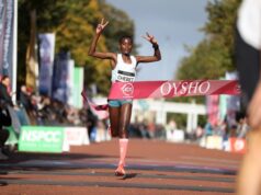 A woman runs through a race finish tape with her arms in the air