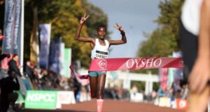 A woman runs through a race finish tape with her arms in the air