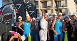 A group of women in trisuits wait at the start of the swim - they look jovial and are smiling at the camera
