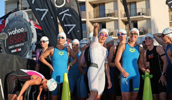 A group of women in trisuits wait at the start of the swim - they look jovial and are smiling at the camera