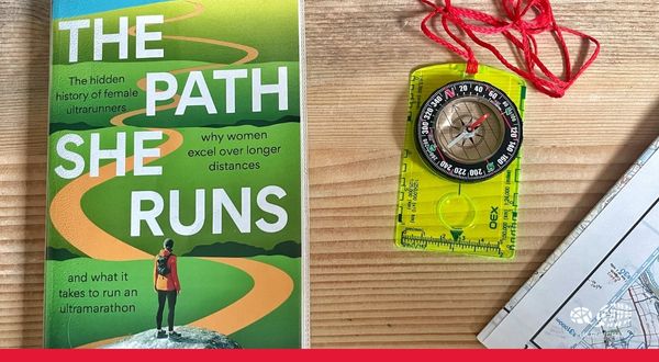 Book Review: The Path She Runs by Jen Benson Photo shows copy of the Path She Runs on a wooden table next to a map and compass
