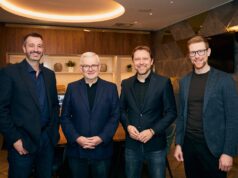 ISPO unite sports and outdoor Industry 4 men all wearing black or dark suits stand in a room and smile for the camera