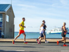 Runners by the coast with a boat in the background out to sea
