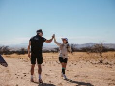 Man in black shorts and T-shirt hi-fives a woman in the desert.
