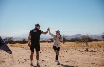British runners break ultra running records in the desert Man in black shorts and T-shirt hi-fives a woman in the desert.