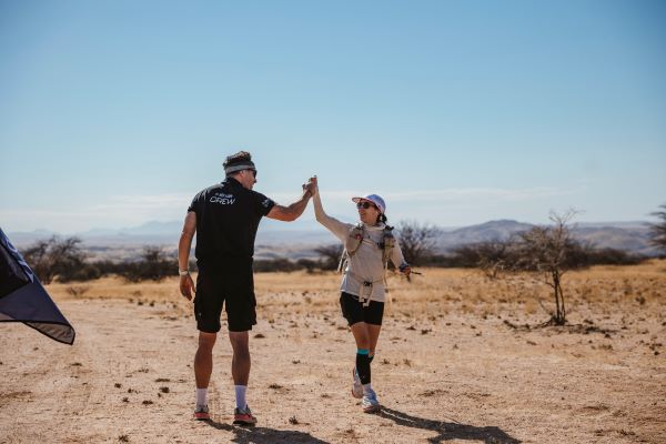 Man in black shorts and T-shirt hi-fives a woman in the desert.