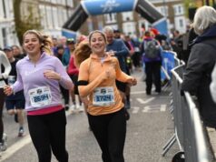 Two young female runners amid a crowd of runners on a busy street