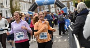 Two young female runners amid a crowd of runners on a busy street