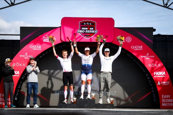 Three men stand on a podium with arms in the air in celebration