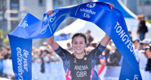 Woman in black tri suit and dark hair lifts blue finish tape aloft