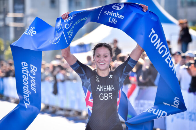 Woman in black tri suit and dark hair lifts blue finish tape aloft