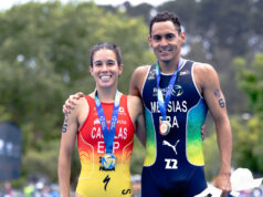A woman and man in tri suits and with medals around their necks pose for the camera together, smiling.