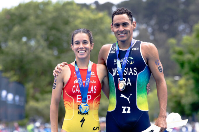 A woman and man in tri suits and with medals around their necks pose for the camera together, smiling.