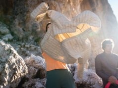 Person puts on a pale grey padded jacket in a rocky location
