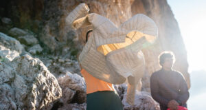 Person puts on a pale grey padded jacket in a rocky location