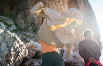 Rab reinvent the Microlight for AW26 Person puts on a pale grey padded jacket in a rocky location