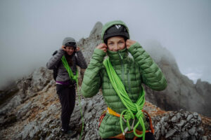 Woman wears a green padded jacket. She has ropes around her waist and torso.
