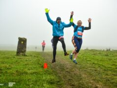 Two runners jump for joy on a grassy trail