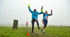 Two runners jump for joy on a grassy trail